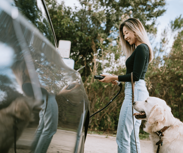 A lady smiling and standing with her dog while recharging her EV via a charging point