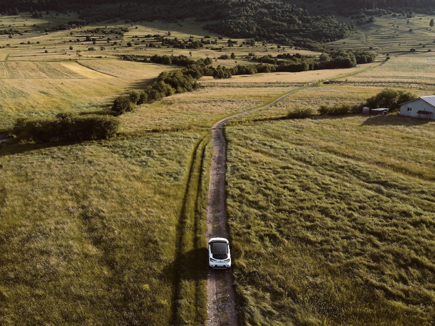 Aerial photo of an electric car driving down a country dirt road.