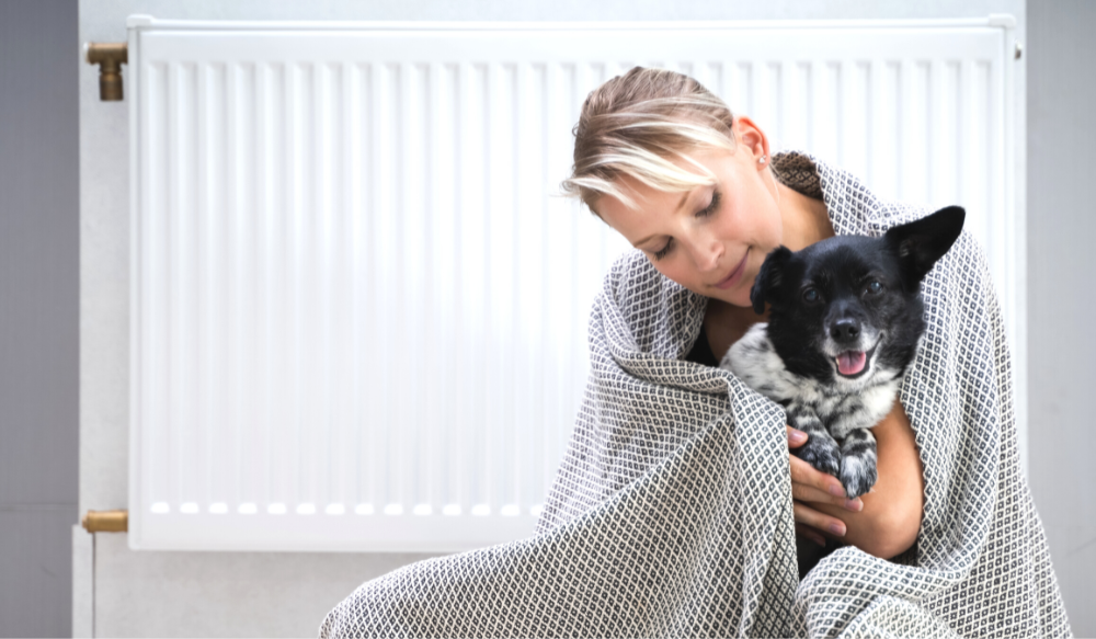 Woman and dog staying warm in winter by the heater